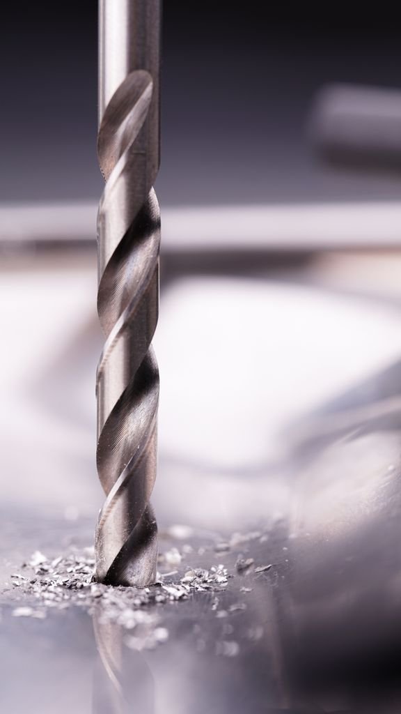 Detailed close-up of a steel drill bit cutting through metal surface, showcasing metalworking precision.