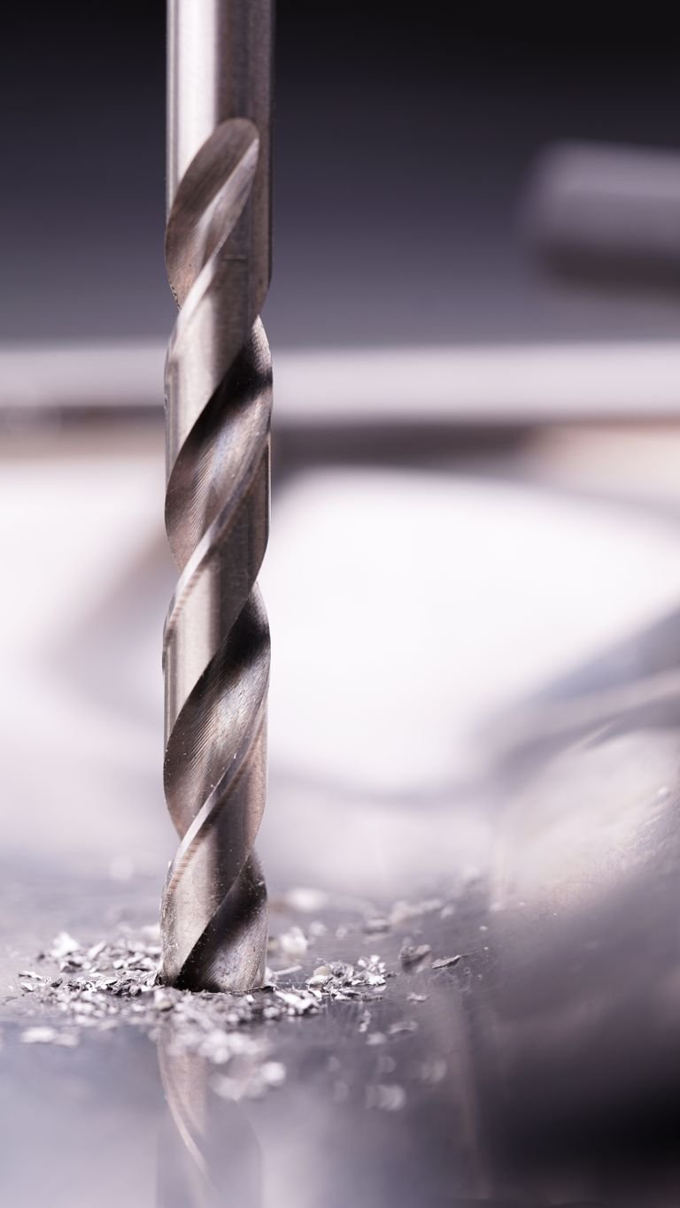 Detailed close-up of a steel drill bit cutting through metal surface, showcasing metalworking precision.
